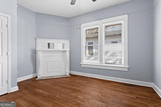 spare room with a ceiling fan, visible vents, baseboards, and wood finished floors