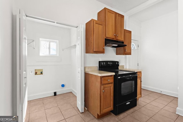 kitchen with light tile patterned floors, under cabinet range hood, light countertops, brown cabinets, and black electric range oven