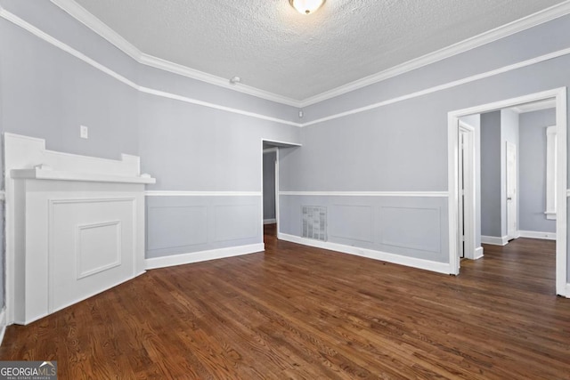 empty room featuring a textured ceiling, ornamental molding, wood finished floors, and wainscoting