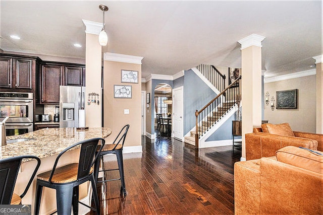 kitchen featuring dark wood-style floors, a breakfast bar area, stainless steel appliances, open floor plan, and ornate columns