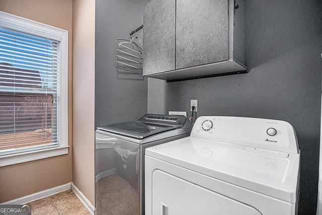 clothes washing area featuring separate washer and dryer, cabinet space, and baseboards