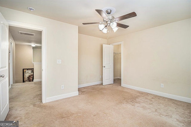 unfurnished bedroom with a walk in closet, light carpet, visible vents, and baseboards