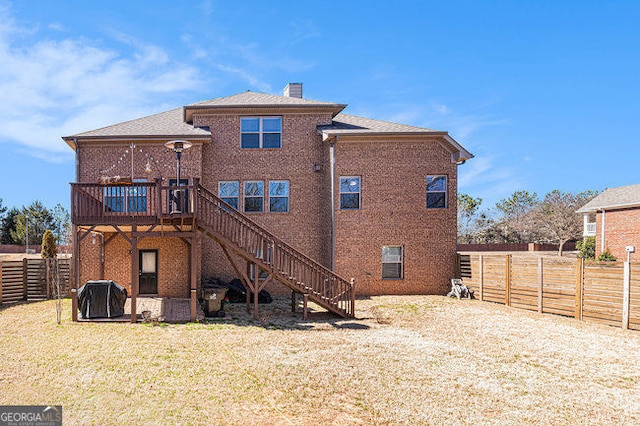 back of property with a fenced backyard, a chimney, stairs, a wooden deck, and brick siding