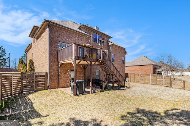 rear view of property featuring brick siding, a yard, a deck, a fenced backyard, and stairs