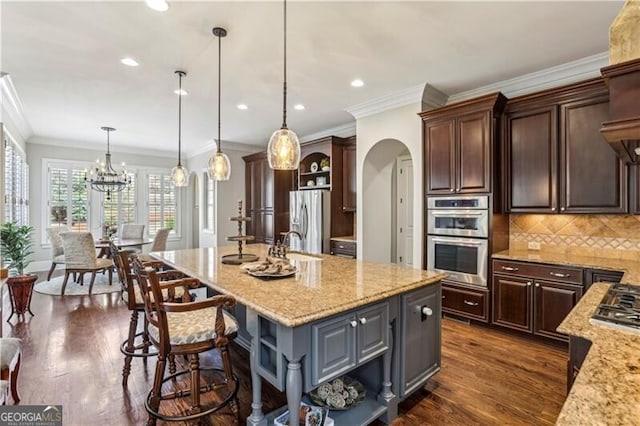 kitchen featuring arched walkways, dark wood finished floors, open shelves, appliances with stainless steel finishes, and an island with sink