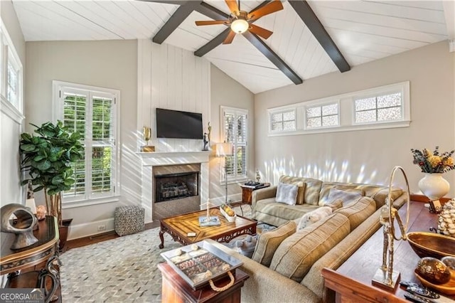 living area featuring lofted ceiling with beams, ceiling fan, a fireplace, wood finished floors, and baseboards