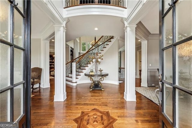 entrance foyer with a towering ceiling, decorative columns, crown molding, and wood finished floors