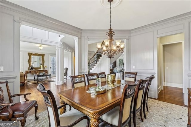 dining space featuring light wood-type flooring, a decorative wall, ornate columns, and an inviting chandelier