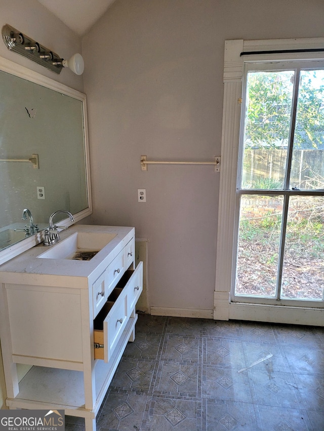 bathroom with plenty of natural light, baseboards, vaulted ceiling, and vanity
