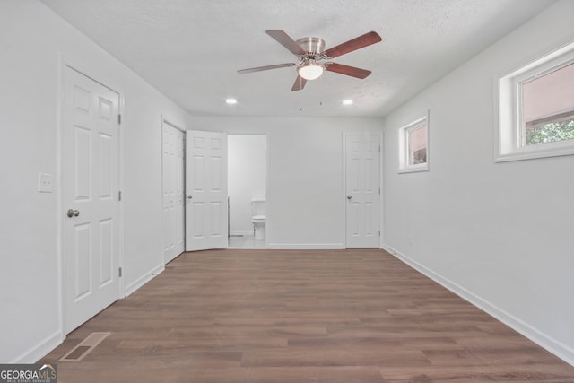 unfurnished bedroom with baseboards, visible vents, dark wood finished floors, and connected bathroom