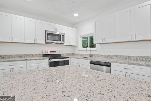 kitchen with stainless steel appliances, white cabinets, a sink, and light stone counters