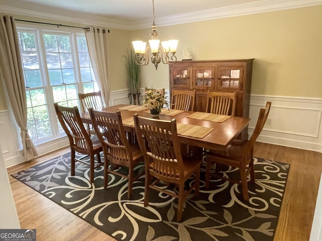 dining space with ornamental molding, a wainscoted wall, a notable chandelier, and wood finished floors