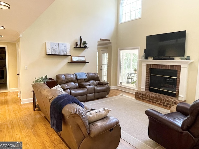 living room featuring light wood-type flooring, baseboards, a fireplace, and a high ceiling