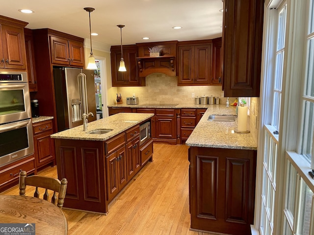 kitchen with hanging light fixtures, light wood-style flooring, backsplash, appliances with stainless steel finishes, and a sink