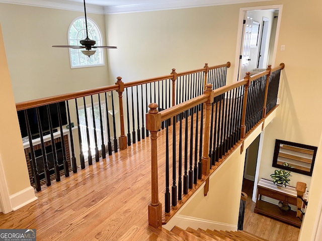 stairway featuring baseboards, ceiling fan, ornamental molding, and wood finished floors