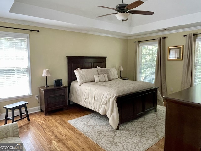 bedroom featuring light wood-style floors, a raised ceiling, visible vents, and crown molding