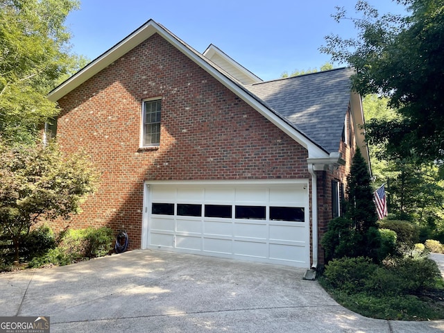 view of home's exterior with concrete driveway, brick siding, and roof with shingles