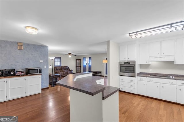 kitchen with stainless steel appliances, dark countertops, white cabinetry, wood finished floors, and under cabinet range hood