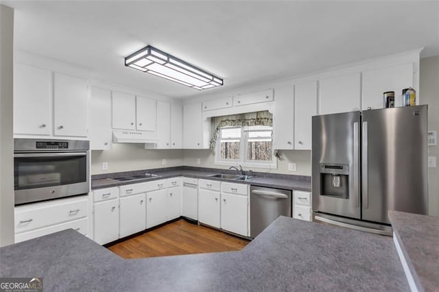 kitchen with stainless steel appliances, dark countertops, white cabinetry, and under cabinet range hood