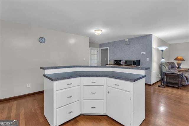 kitchen featuring dark countertops, open floor plan, stainless steel microwave, and wood finished floors