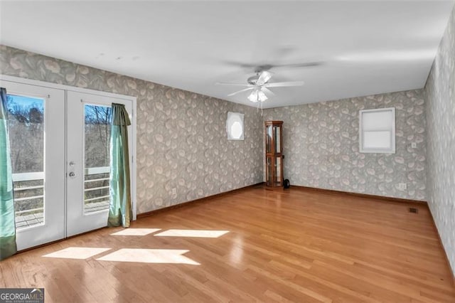 spare room with wood finished floors, french doors, a healthy amount of sunlight, and wallpapered walls