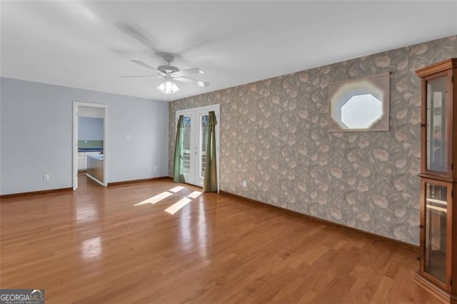 unfurnished living room featuring wallpapered walls, french doors, wood finished floors, and baseboards