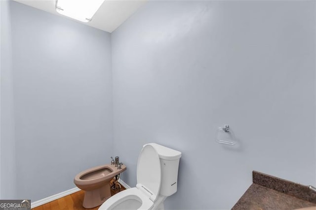 half bathroom with baseboards, a bidet, toilet, and wood finished floors