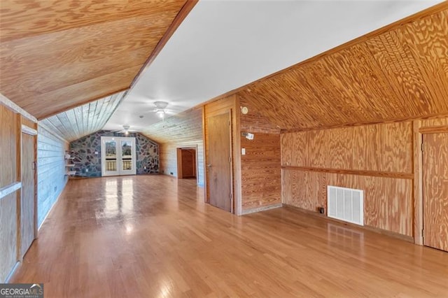 additional living space with visible vents, wooden walls, and wood finished floors