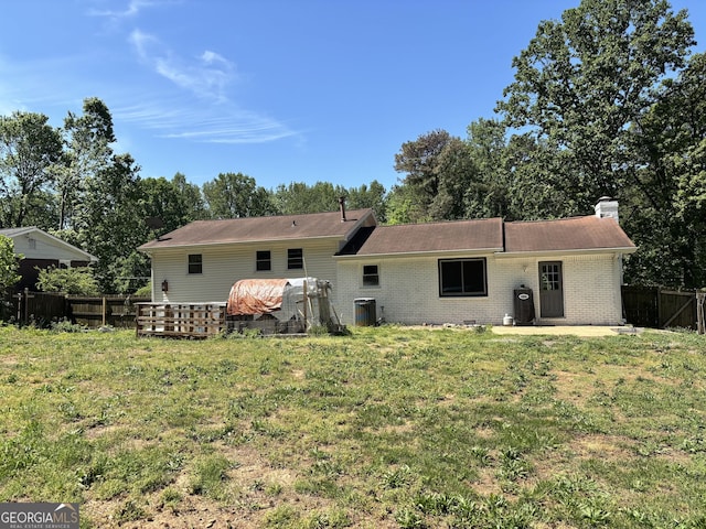 rear view of property featuring central air condition unit, a chimney, fence, brick siding, and a yard