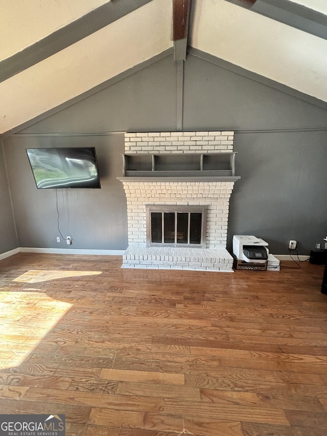 unfurnished living room with baseboards, a brick fireplace, wood finished floors, and vaulted ceiling with beams
