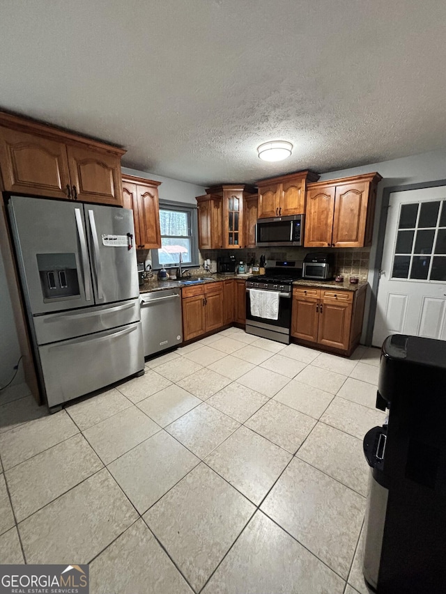 kitchen featuring light tile patterned floors, dark countertops, glass insert cabinets, and appliances with stainless steel finishes