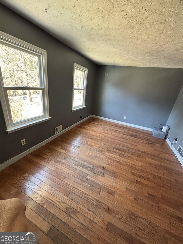 spare room featuring wood-type flooring, baseboards, a textured ceiling, and visible vents