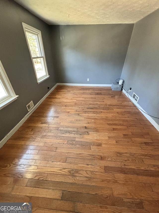 interior space with hardwood / wood-style floors, baseboards, visible vents, and a textured ceiling