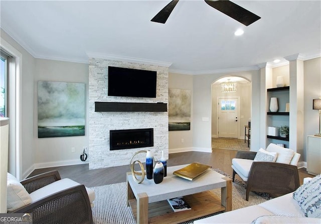 living room with arched walkways, ceiling fan, ornamental molding, wood finished floors, and a fireplace