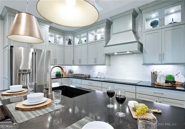 kitchen featuring high quality fridge, black electric cooktop, premium range hood, a sink, and tasteful backsplash