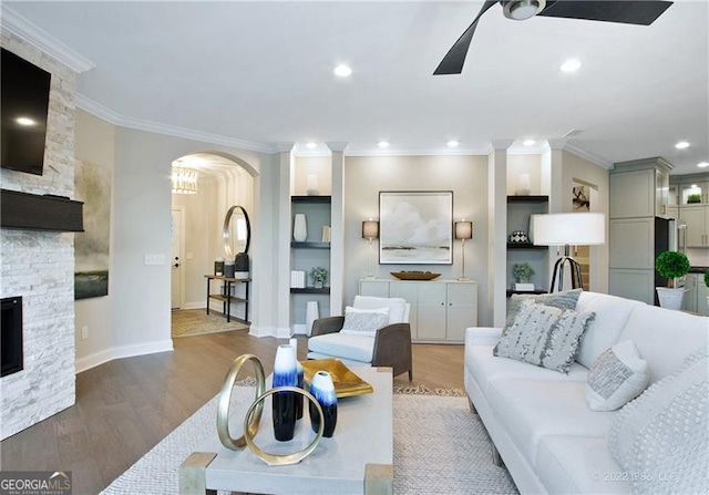 living room with arched walkways, a stone fireplace, wood finished floors, and crown molding