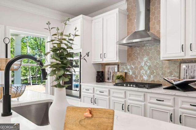 kitchen featuring tasteful backsplash, white cabinets, wall chimney exhaust hood, crown molding, and stainless steel gas cooktop