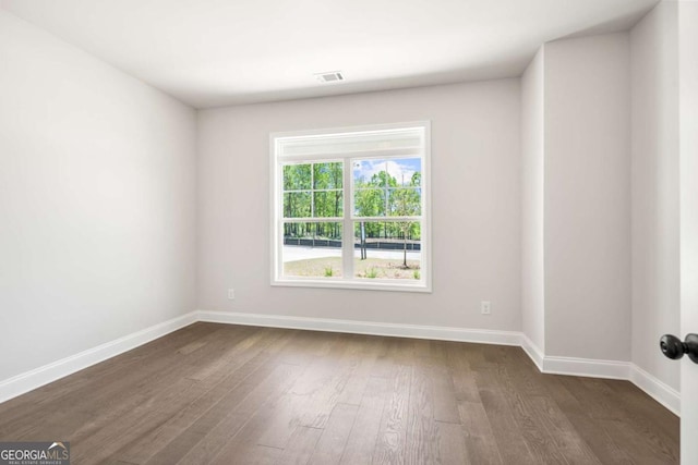 empty room with dark wood-type flooring, visible vents, and baseboards