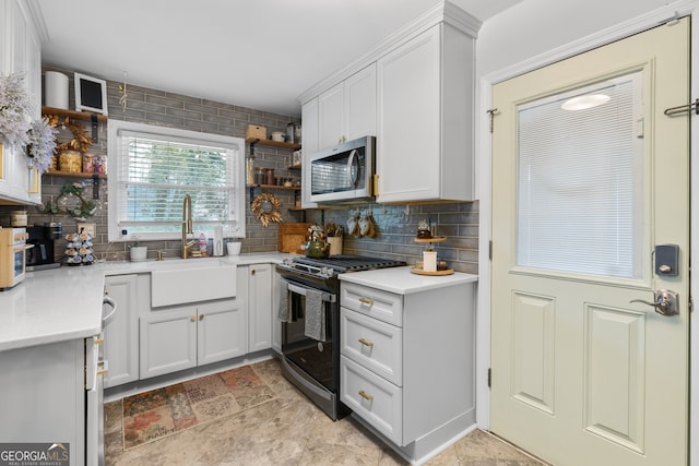 kitchen featuring tasteful backsplash, range with gas stovetop, stainless steel microwave, open shelves, and a sink