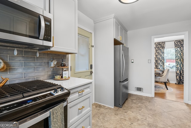 kitchen featuring baseboards, visible vents, stainless steel appliances, light countertops, and backsplash