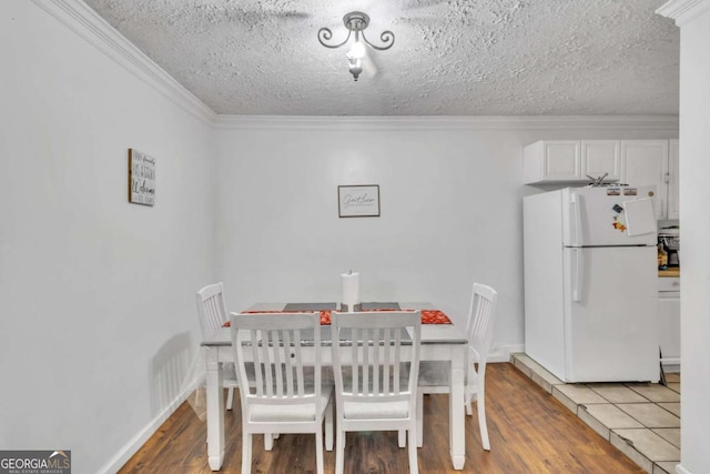 dining area with a textured ceiling, ornamental molding, baseboards, and light wood-style floors