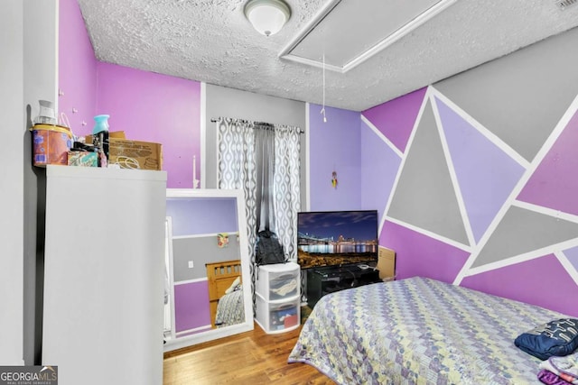 bedroom featuring attic access, a textured ceiling, and wood finished floors