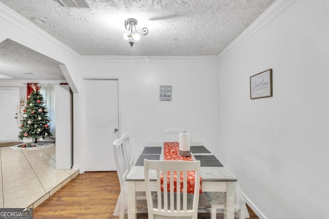 dining area with a textured ceiling, ornamental molding, and wood finished floors