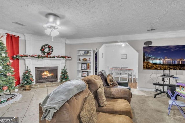 tiled living area featuring built in features, a warm lit fireplace, visible vents, and a textured ceiling