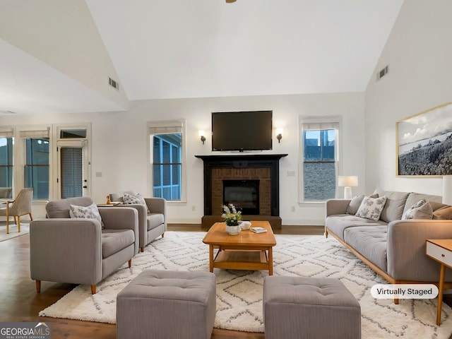 living area with high vaulted ceiling, a fireplace, wood finished floors, and visible vents