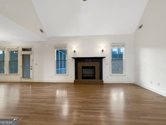 unfurnished living room with a brick fireplace, baseboards, visible vents, and wood finished floors