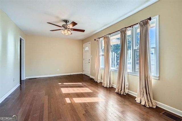 empty room featuring a ceiling fan, dark wood finished floors, visible vents, and baseboards