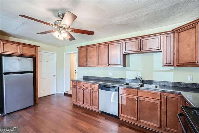 kitchen featuring dark wood-style floors, stainless steel appliances, dark countertops, and a sink