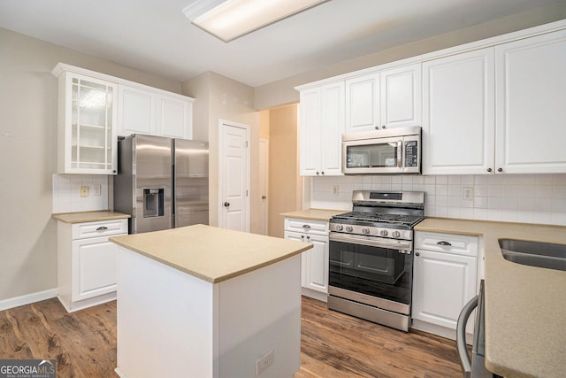 kitchen featuring white cabinets, glass insert cabinets, wood finished floors, stainless steel appliances, and backsplash