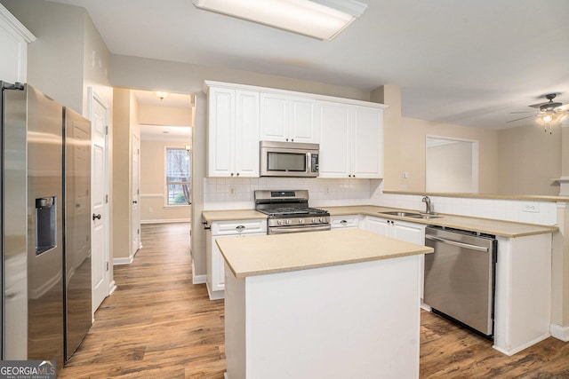 kitchen with light countertops, backsplash, appliances with stainless steel finishes, a sink, and a peninsula